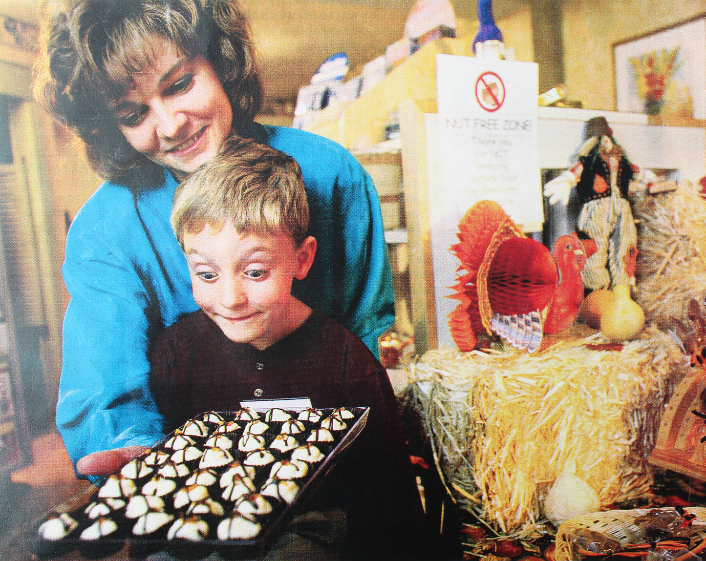 Woman and child admiring a box of truffles. "Nut Free Zone" sign in background.