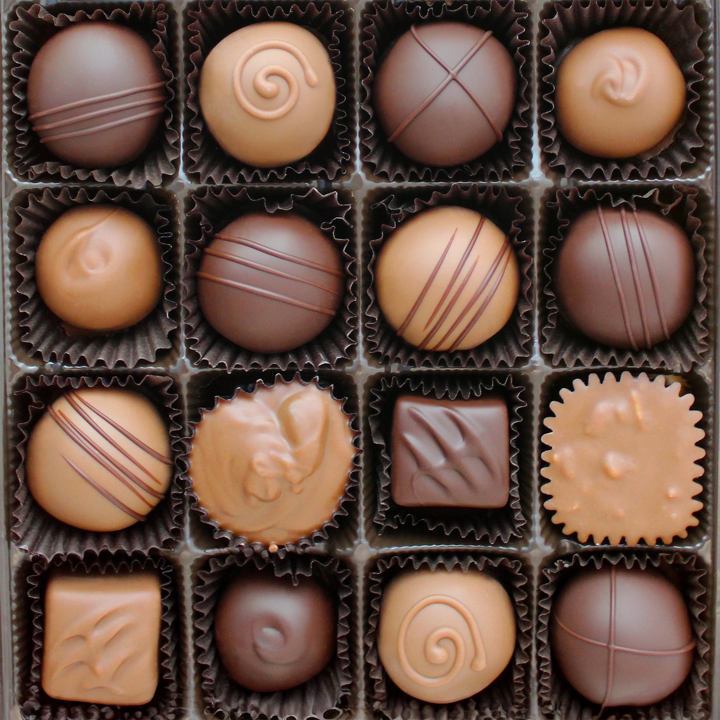 Close up shot of boxed chocolates including truffles, caramels, raisin clusters, buttercreams, and crispy cups