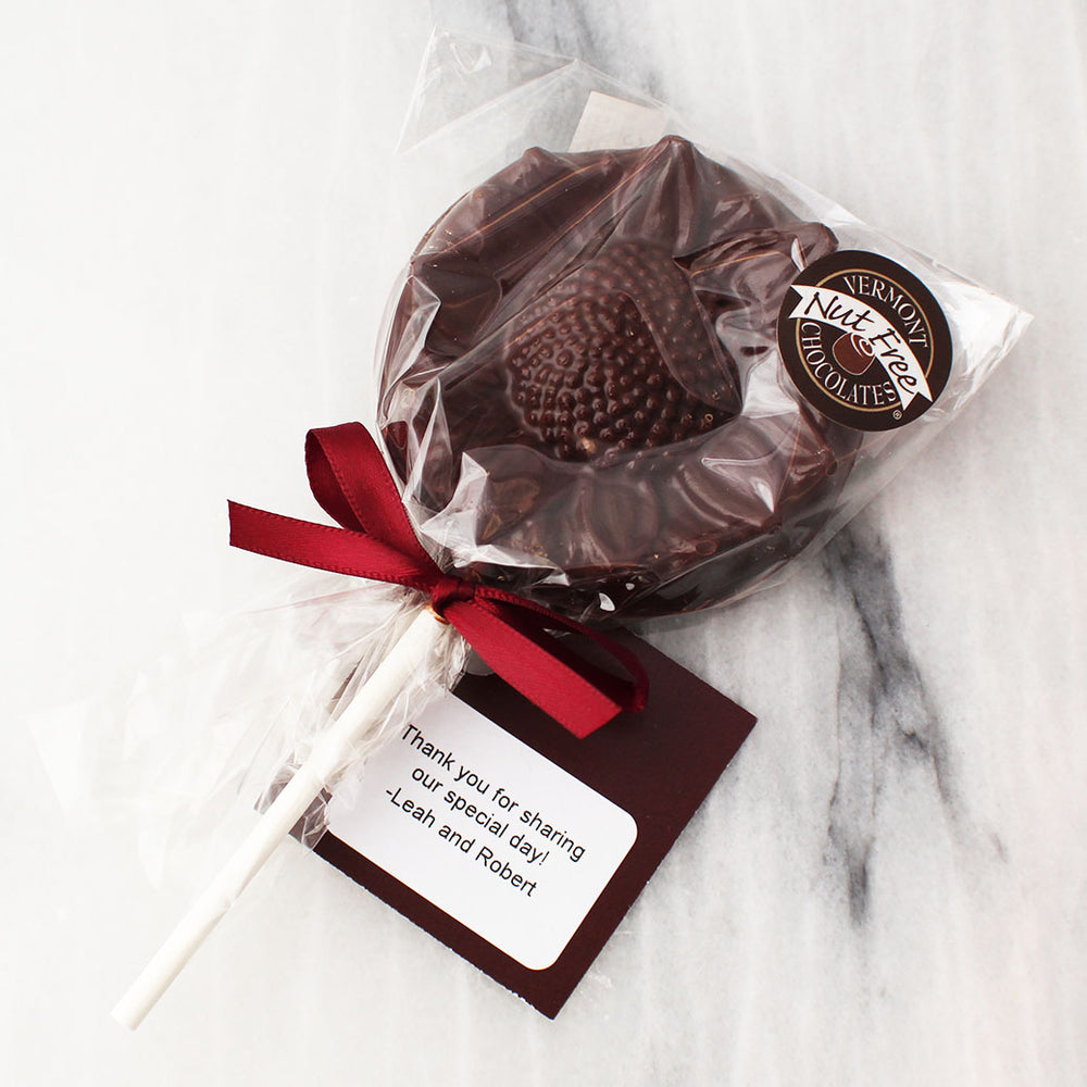 Dark chocolate sun flower shape on a popsicle stick. Adorned with red ribbon and a card that says "Thank you for sharing our special day!" -Leah and Robert