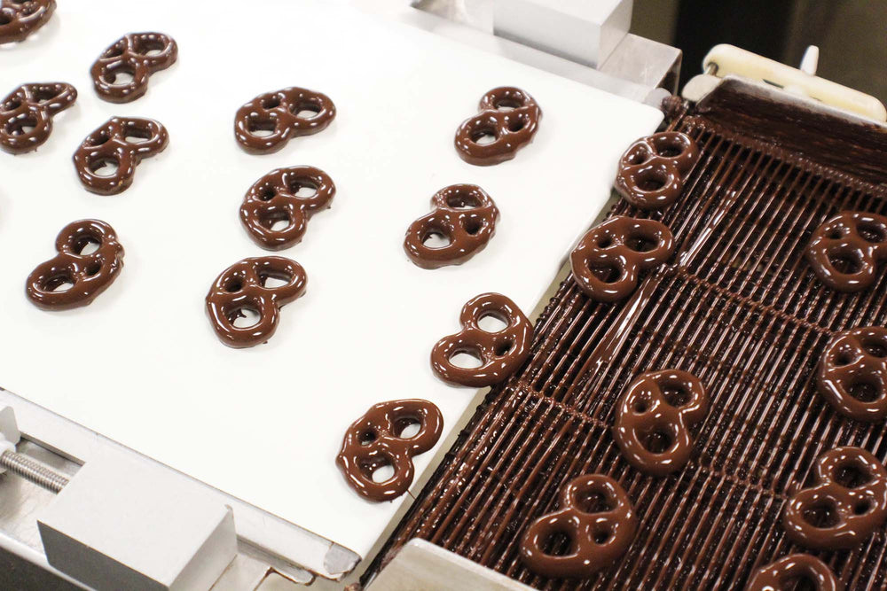Dark chocolate covered mini twist pretzels on conveyor belt. 