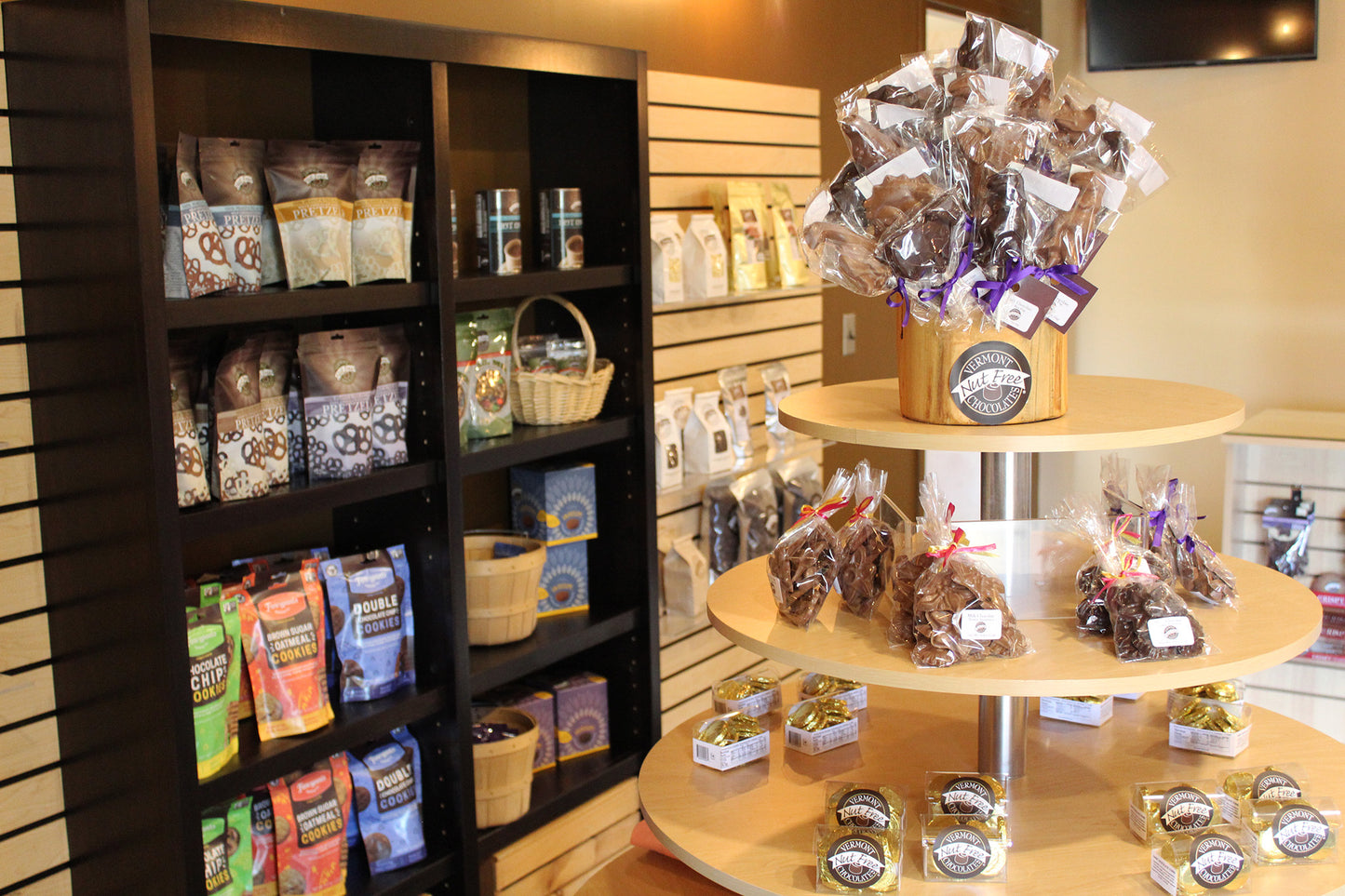 Inside of Vermont Nut Free Chocolates factory store. Shelves with bags of product. Table filled with smaller bags of product and chocolate pops.
