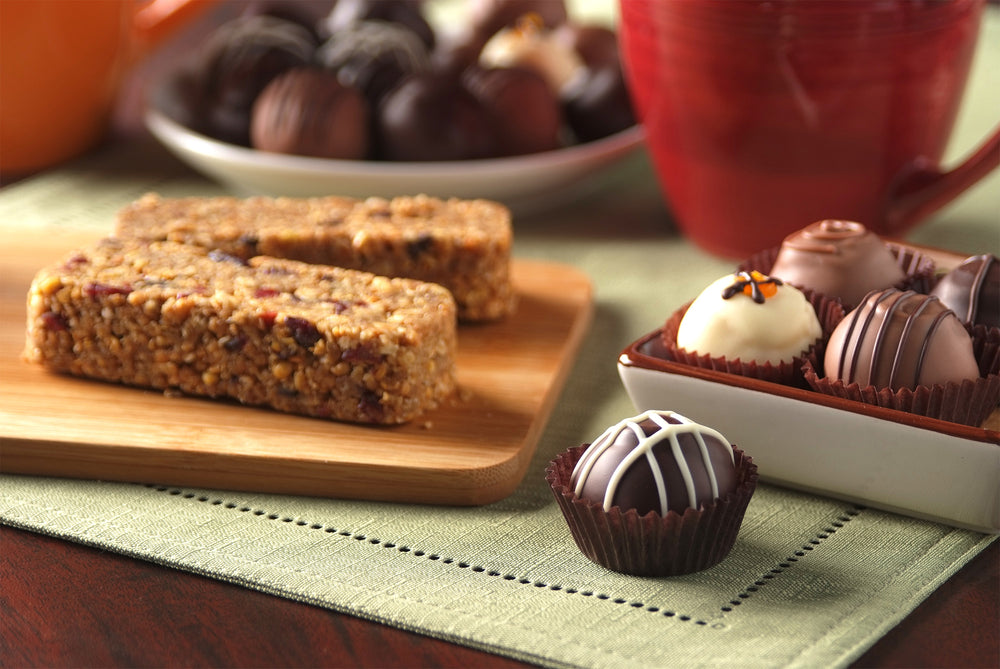 TANABAR Granola Bars and an assortment of nut free truffles on a table top. Featuring green fabric place setting  and red mug.