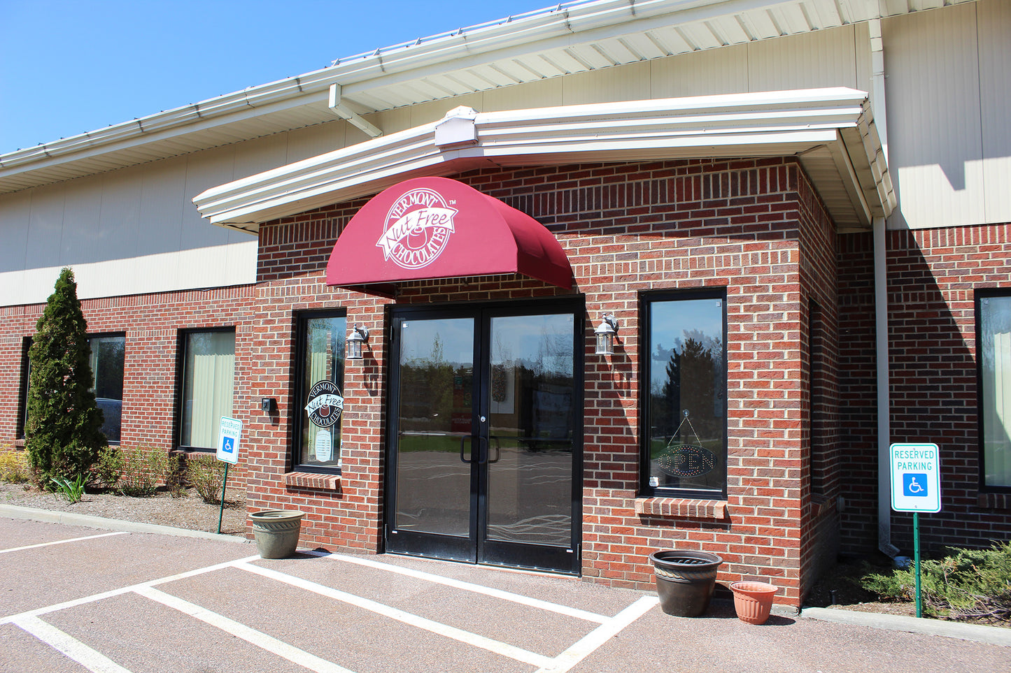 Front of Vermont Nut Free Chocolates factory store. Brick building with red awning. White Vermont Nut Free Chocolates logo on awning.